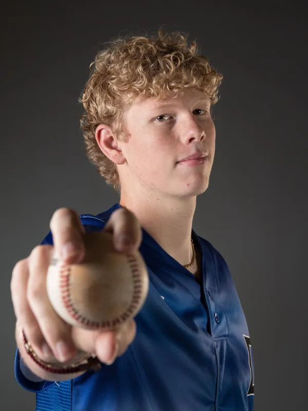 Baseball player holding ball, wearing blue jersey.